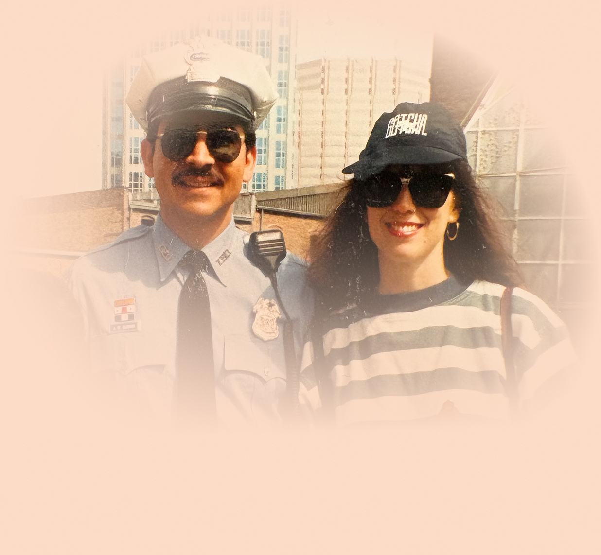 Snapshot of a police officer and a smiling woman in sunglasses posing together outside a building.
